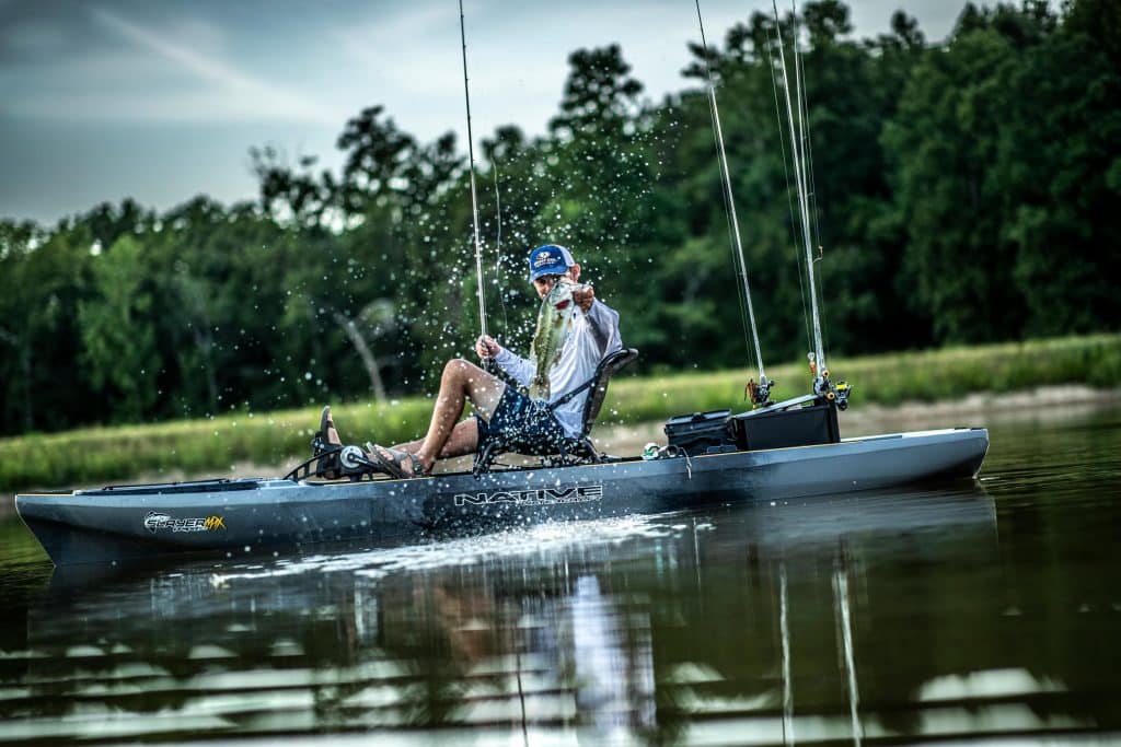 Ein Angler sitzt auf einem Kajak und hält einen Fang über dem Wasser, während Spritzer um ihn herum aufsteigen.
